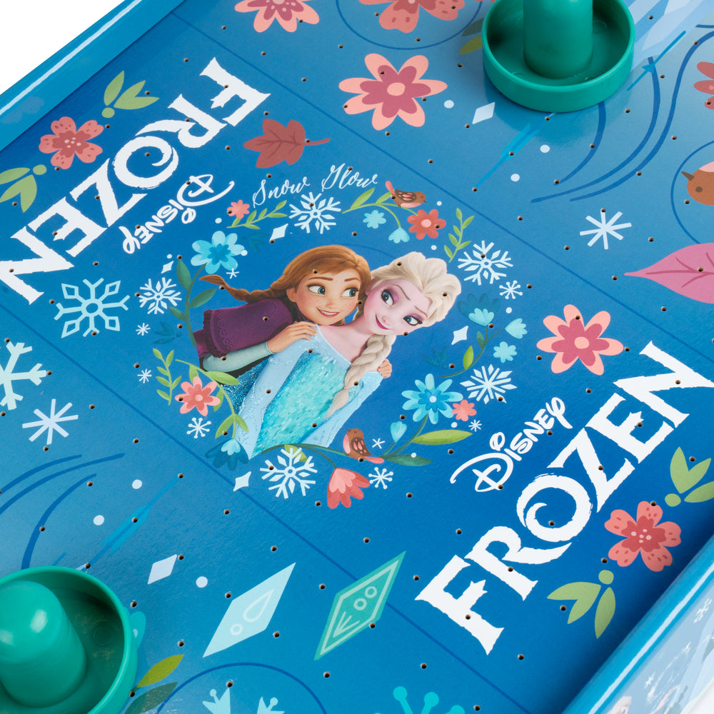 Close-up of a Disney Frozen-themed board game surface in bright blue, decorated with floral graphics, snowflakes, and character artwork of Anna and Elsa. Green game pieces are partially visible at the top and bottom edges.