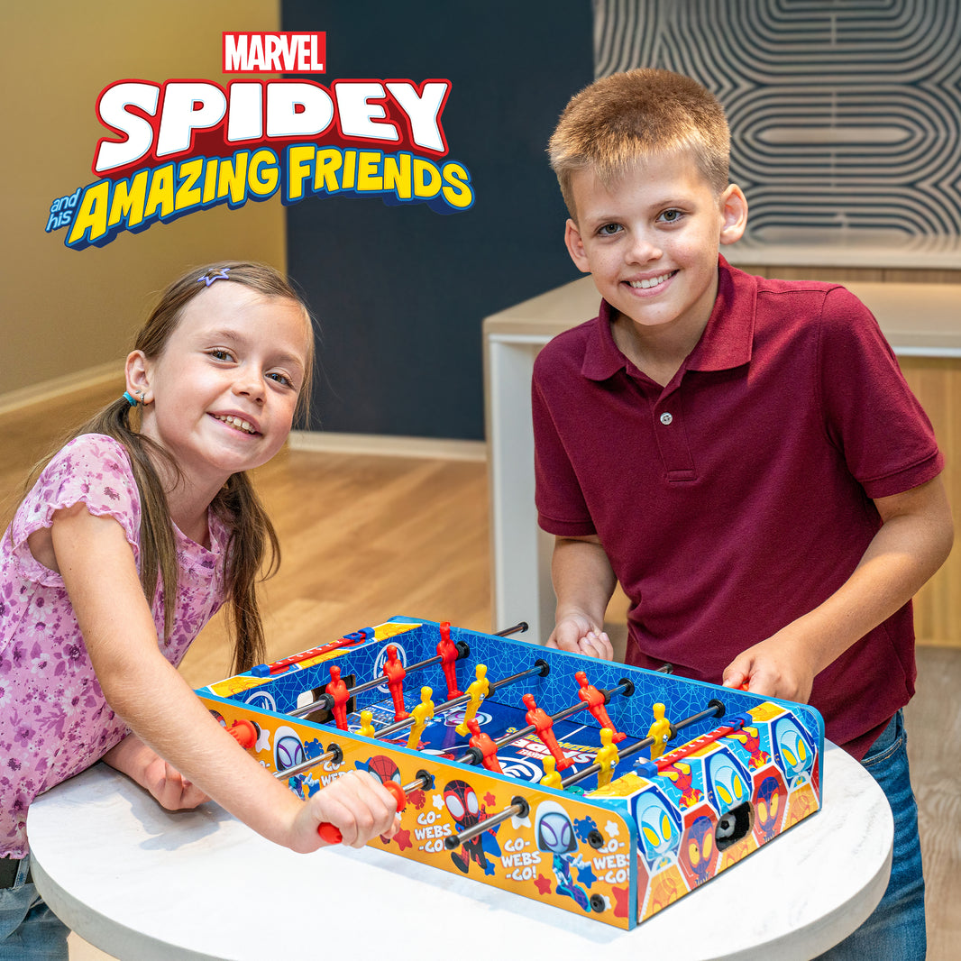 Two children playing with a Marvel Spider-Man foosball table in a room.