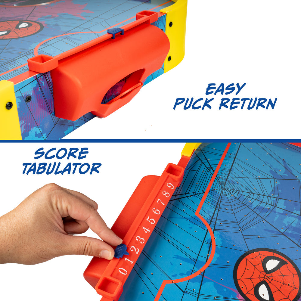 Close-up of a Spider-Man-themed arcade game with an orange return slot labeled 'EASY PUCK RETURN' and a hand using a score tabulator labeled 'SCORE TABULATOR' on a blue web-pattern board.