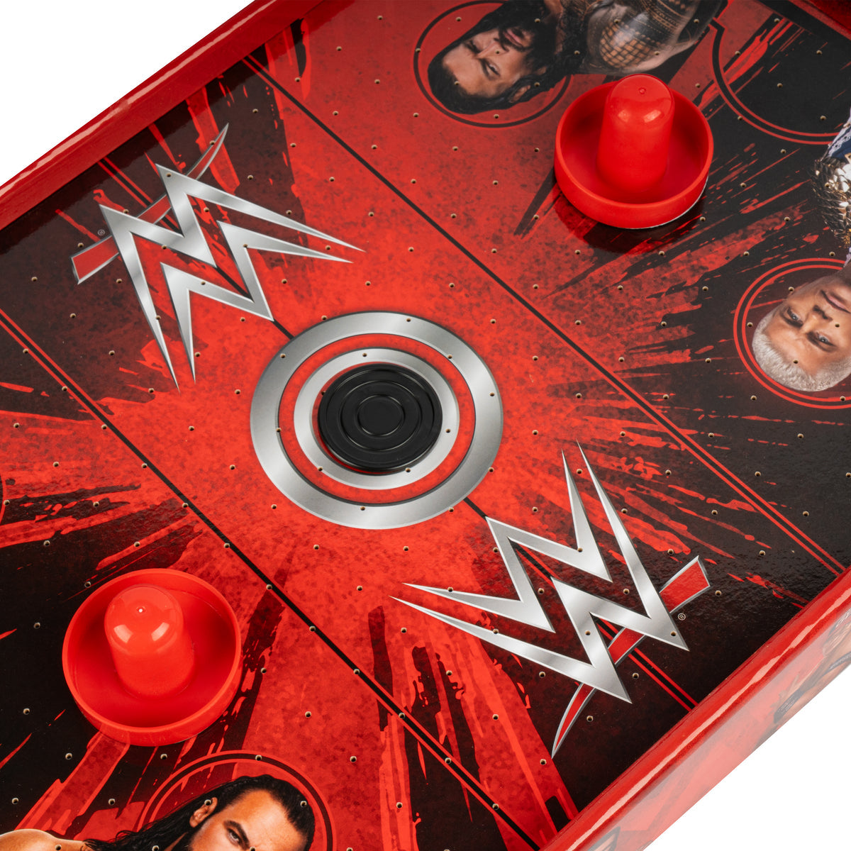 Close-up of a WWE-themed air hockey table with red and black graphics, silver WWE logos, player portraits, and red discs on a white background.